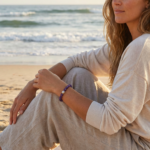 A woman wearing a crystal bracelet while sitting by the ocean, capturing a peaceful and reflective lifestyle moment.