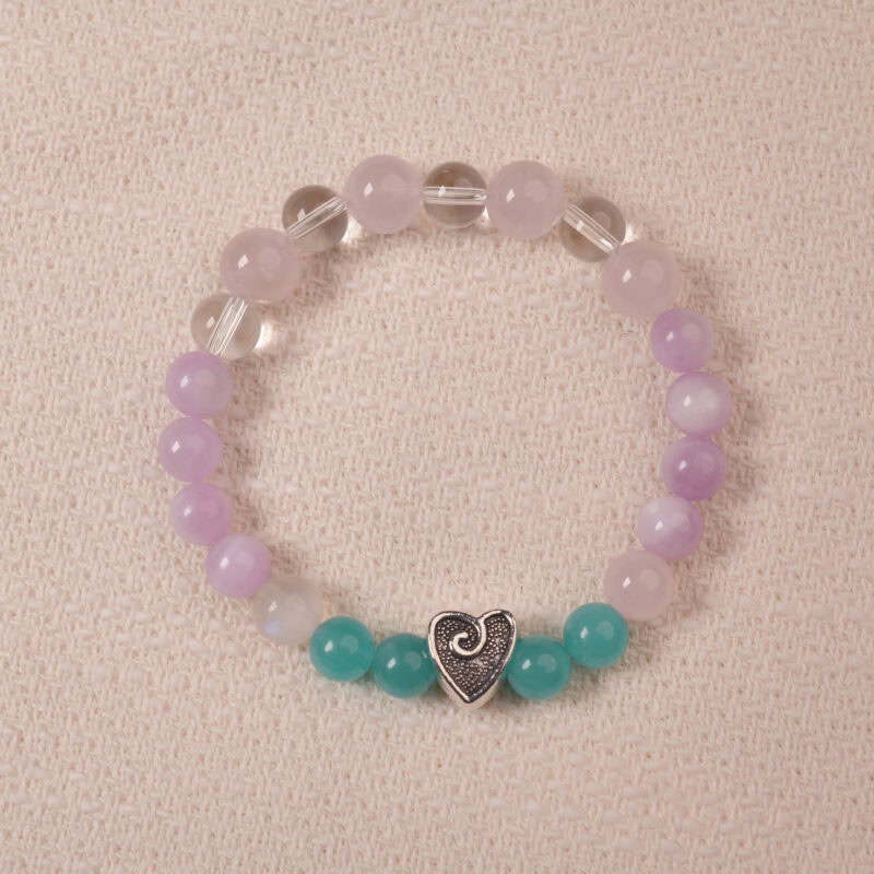 Amethyst and Prehnite bracelet featuring smooth, polished beads in shades of purple and green, with a central silver heart-shaped bead. The bracelet is displayed on a soft fabric surface, emphasizing its elegance and soothing colors.