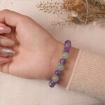 A hand wearing the Amethyst and Prehnite bracelet, featuring purple Amethyst and green Prehnite beads. The bracelet is paired with a soft beige sweater and delicate nails, adding a chic and peaceful vibe.