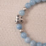 Close-up of silver heart charm with star engravings on aquamarine bracelet.