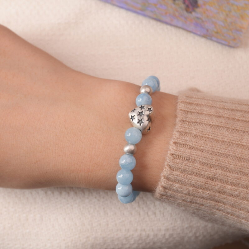 Model wearing aquamarine bracelet with silver heart charm, showing elegant blue tone and serene energy.