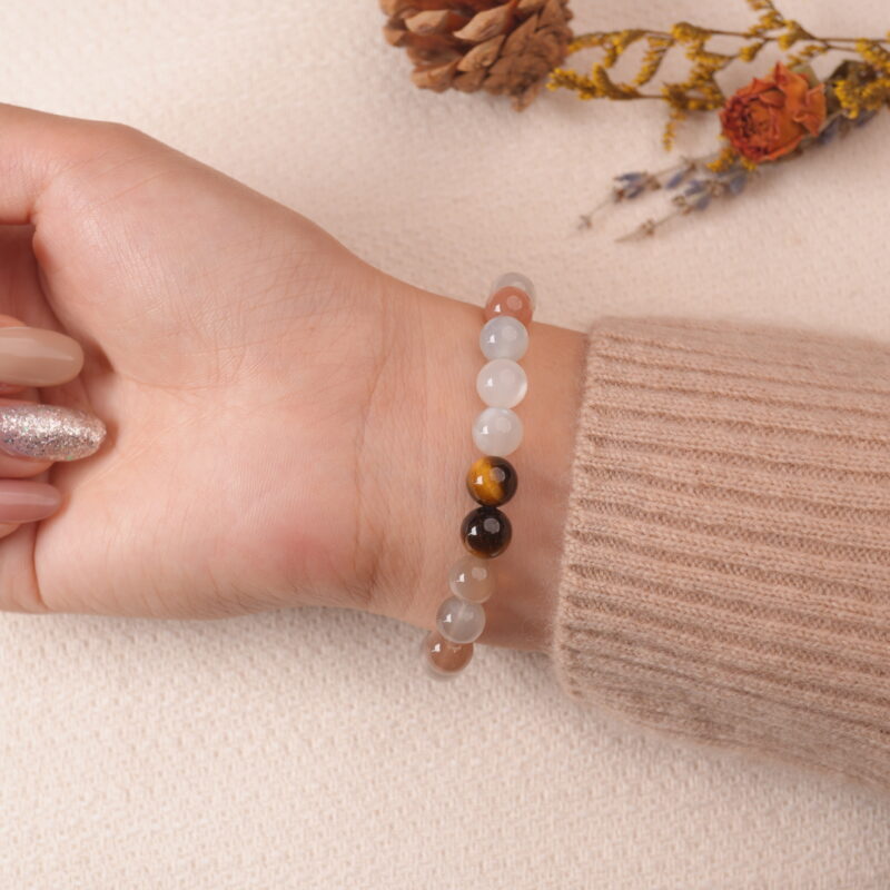 A close-up shot of a hand wearing a Rainbow Moonstone bracelet with a silver heart charm engraved with "I love you". The bracelet features soft, iridescent moonstone beads and is paired with a cozy beige sweater, adding a touch of elegance and warmth.