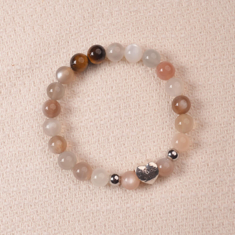 Rainbow moonstone and tiger’s eye bracelet with a silver heart bead engraved with “I love you,” photographed under soft daylight to highlight the iridescent white and golden-brown hues.