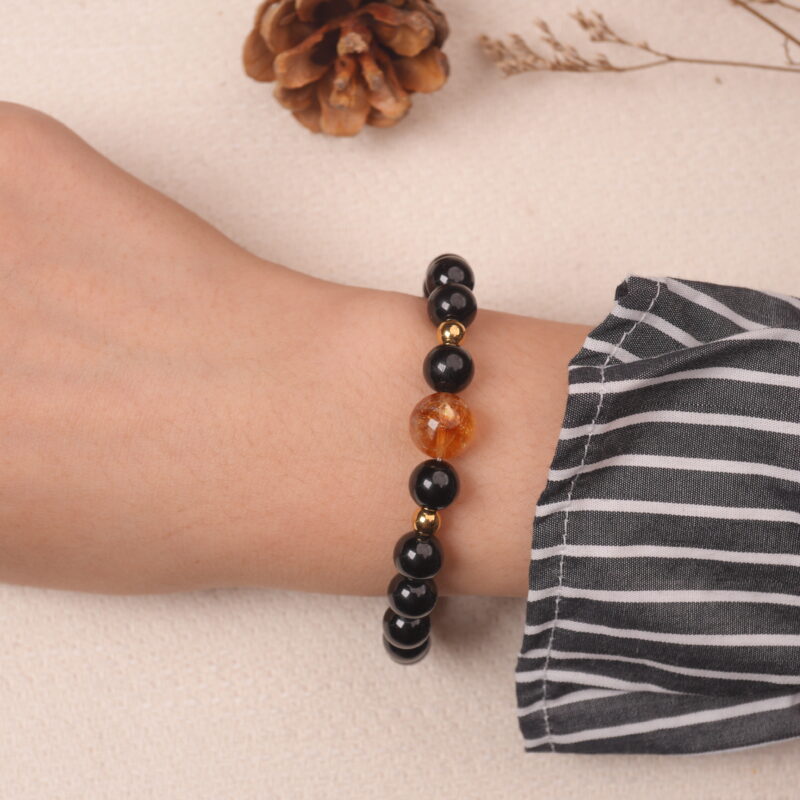 A hand wearing the Obsidian, Citrine, and Moonstone bracelet. The combination of black, gold, and iridescent stones creates a stunning and energetic look on the wrist.