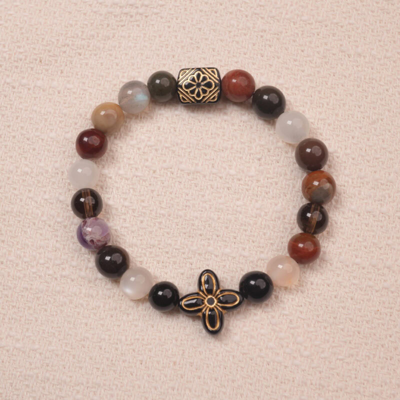 Multicolor gemstone bracelet with a black and gold patterned bead, photographed under soft daylight on a neutral background.