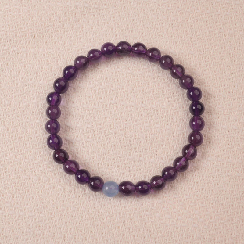 A close-up of an Amethyst and Aquamarine bracelet, featuring polished purple Amethyst beads and a single pale blue Aquamarine bead. The combination of rich purple and light blue creates a calming and balanced look.