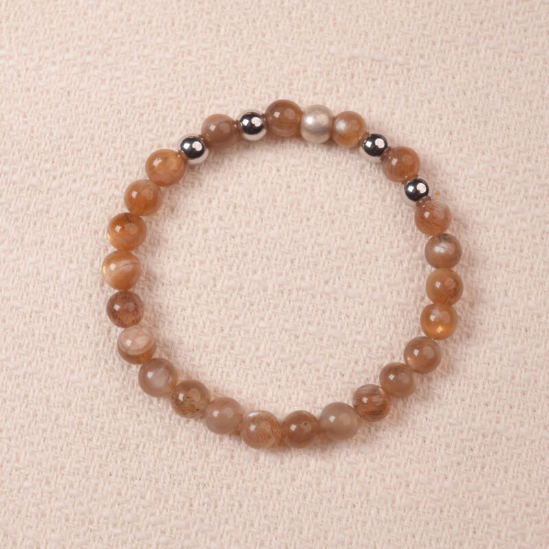 A close-up of a Peach Moonstone bracelet, featuring smooth, polished beads in warm orange tones. The bracelet is accented with silver spacer beads, creating a harmonious contrast between the gemstones.