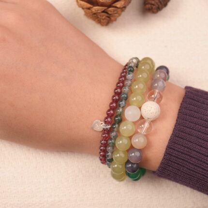 Worn multi-gemstone bracelet stack for good luck, featuring green, white, and red-toned beads