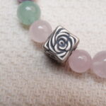 Close-up detail of the silver rose charm on a bracelet made of rose quartz, amethyst, and green aventurine beads.