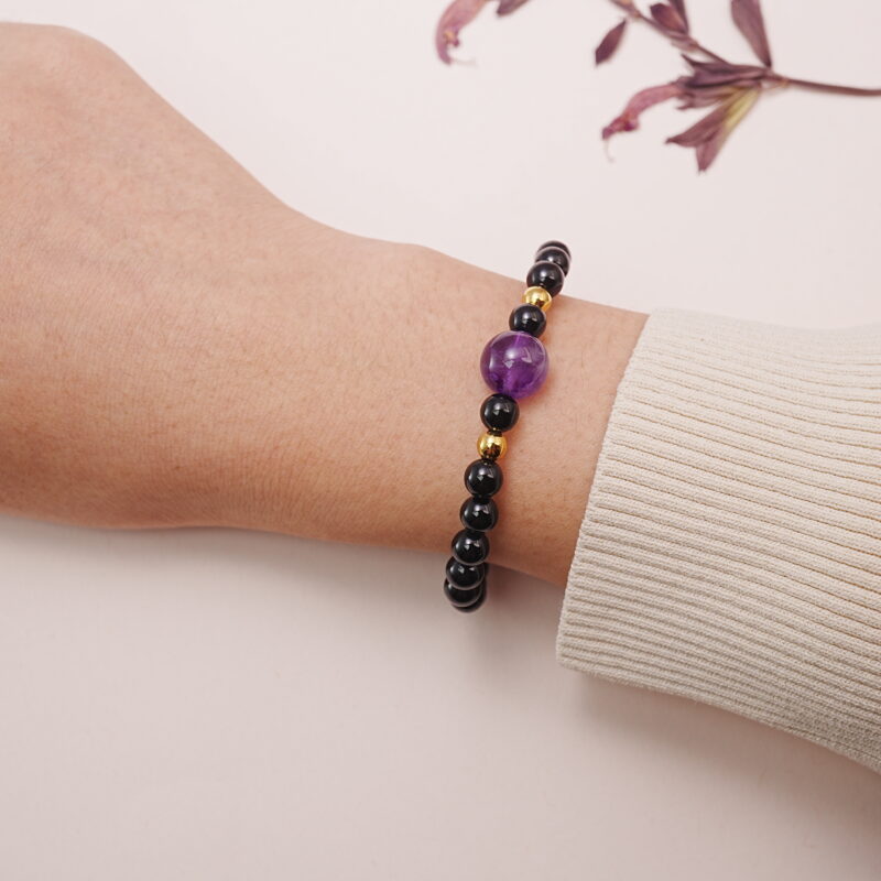 Close-up wrist shot of obsidian and amethyst bracelet with gold accents