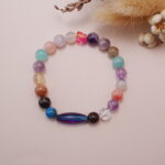 Styled scene image of a colorful multi-gemstone bracelet with various natural crystal beads arranged on a soft backdrop.