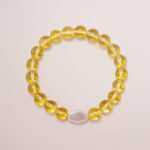 Yellow glass bead bracelet with a white oval accent charm displayed on a soft pink background.