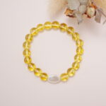 Yellow glass bead bracelet with a white oval accent placed beside dried flowers on a soft surface.