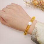 Yellow glass bead bracelet with a white oval charm worn on the wrist, styled with a floral sleeve.