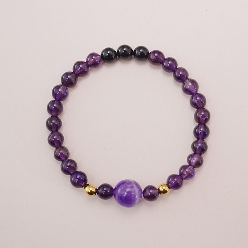 Amethyst and black tourmaline bracelet with gold accent beads, photographed under soft daylight on a neutral background.
