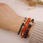Protective multi-strand bracelet stack styled on wrist with warm and dark beads.