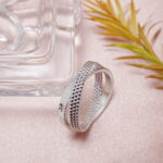 S925 textured band ring placed beside clear glass decor on pink surface