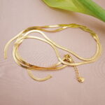 Long chain necklace styled beside a tulip on soft pink fabric