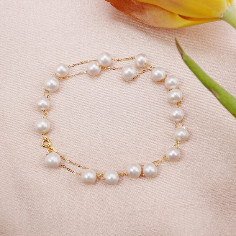 Pearl bracelet with gold chain arranged beside yellow flower on pink fabric