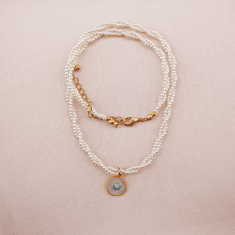 Single-strand pearl necklace with a gold round pendant displayed on a soft pink background.