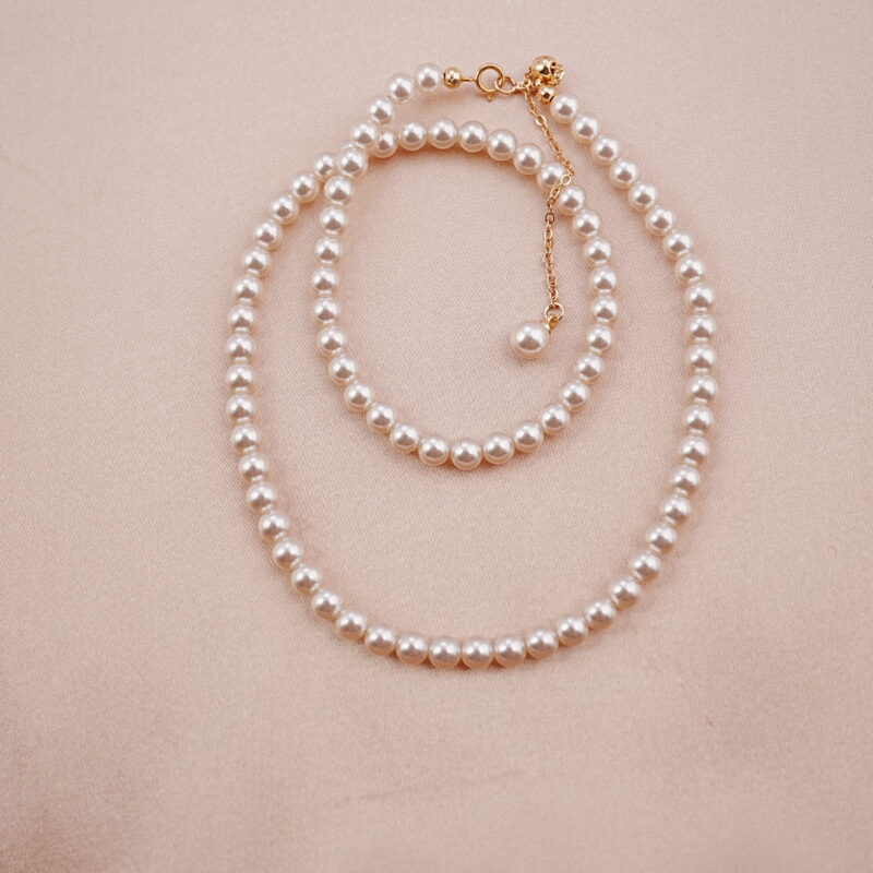 Elegant single-strand pearl necklace with gold clasp displayed on soft pink background