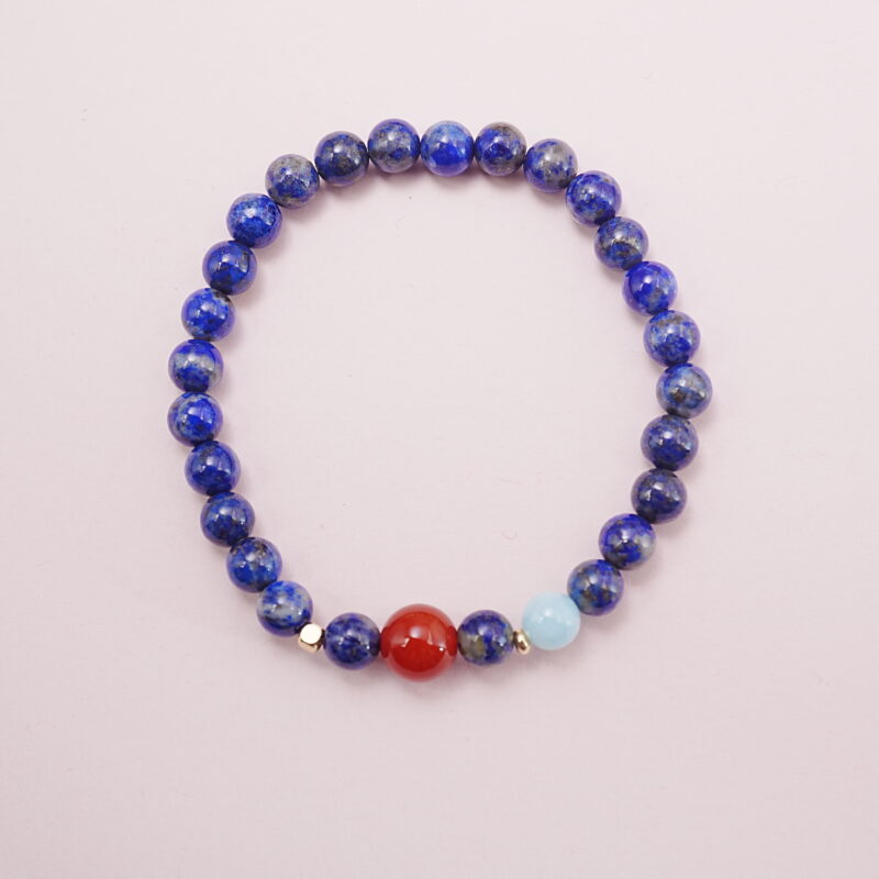 Lapis lazuli bracelet with a carnelian accent bead and aquamarine charm displayed on a soft background.