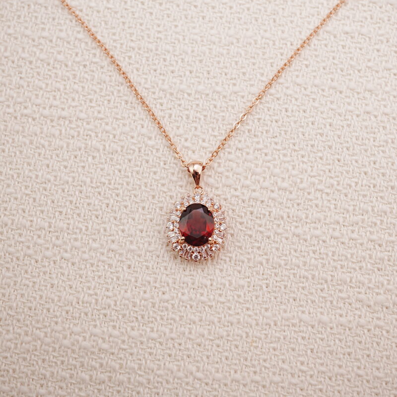 Ruby halo pendant necklace in rose gold displayed on a soft beige background.
