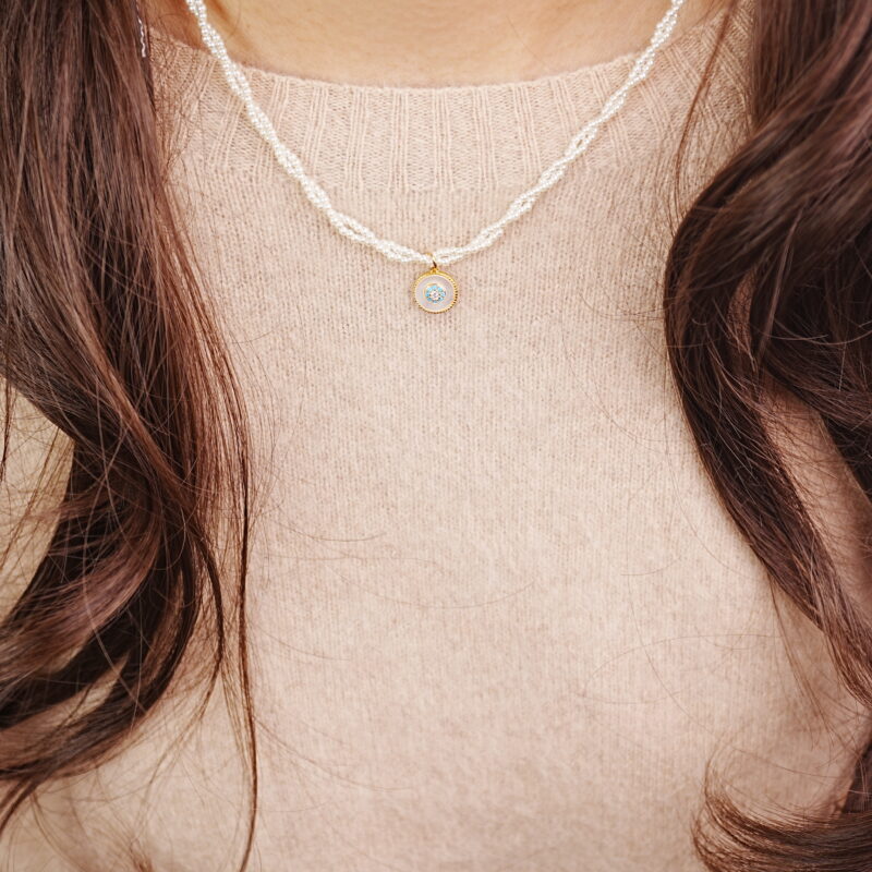 Model wearing a single-strand pearl necklace with a gold round pendant.