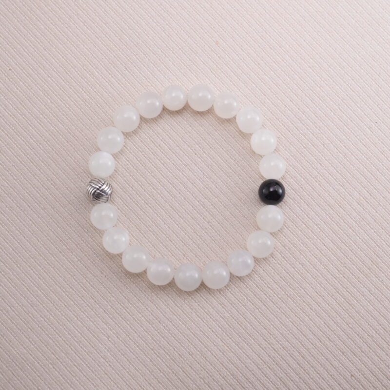 White moonstone beaded bracelet with a single black obsidian accent bead, displayed on a soft beige background.