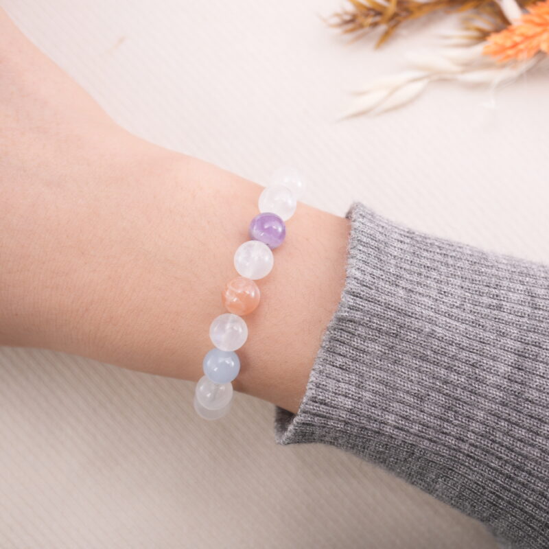 White Moonstone bracelet with light blue, peach, and purple beads shown on wrist.