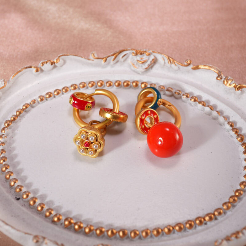 Colorful hoop earrings with red bead and flower-shaped charm displayed on a decorative plate