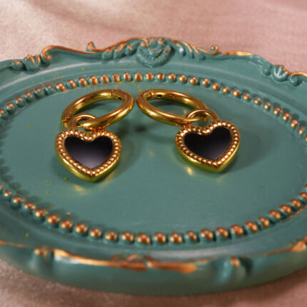 Heart-shaped black enamel hoop earrings displayed on a decorative teal tray