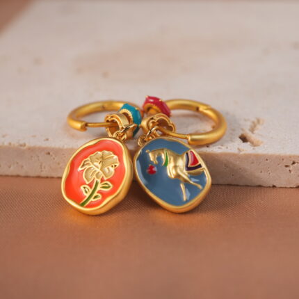 A pair of horse-shaped enamel earrings in vibrant red displayed neatly on a jewelry card.