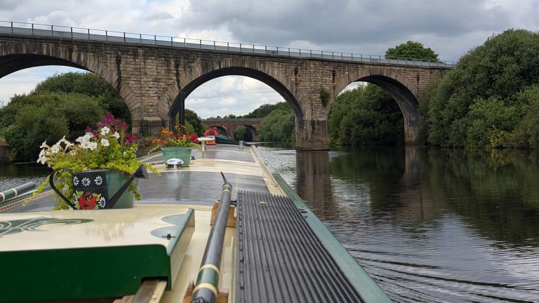 Narrowboat cruising under a historic stone bridge on a calm river in the UK.
