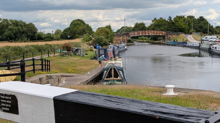 Narrowboat navigating the canal with lush green surroundings and a bridge in the background.