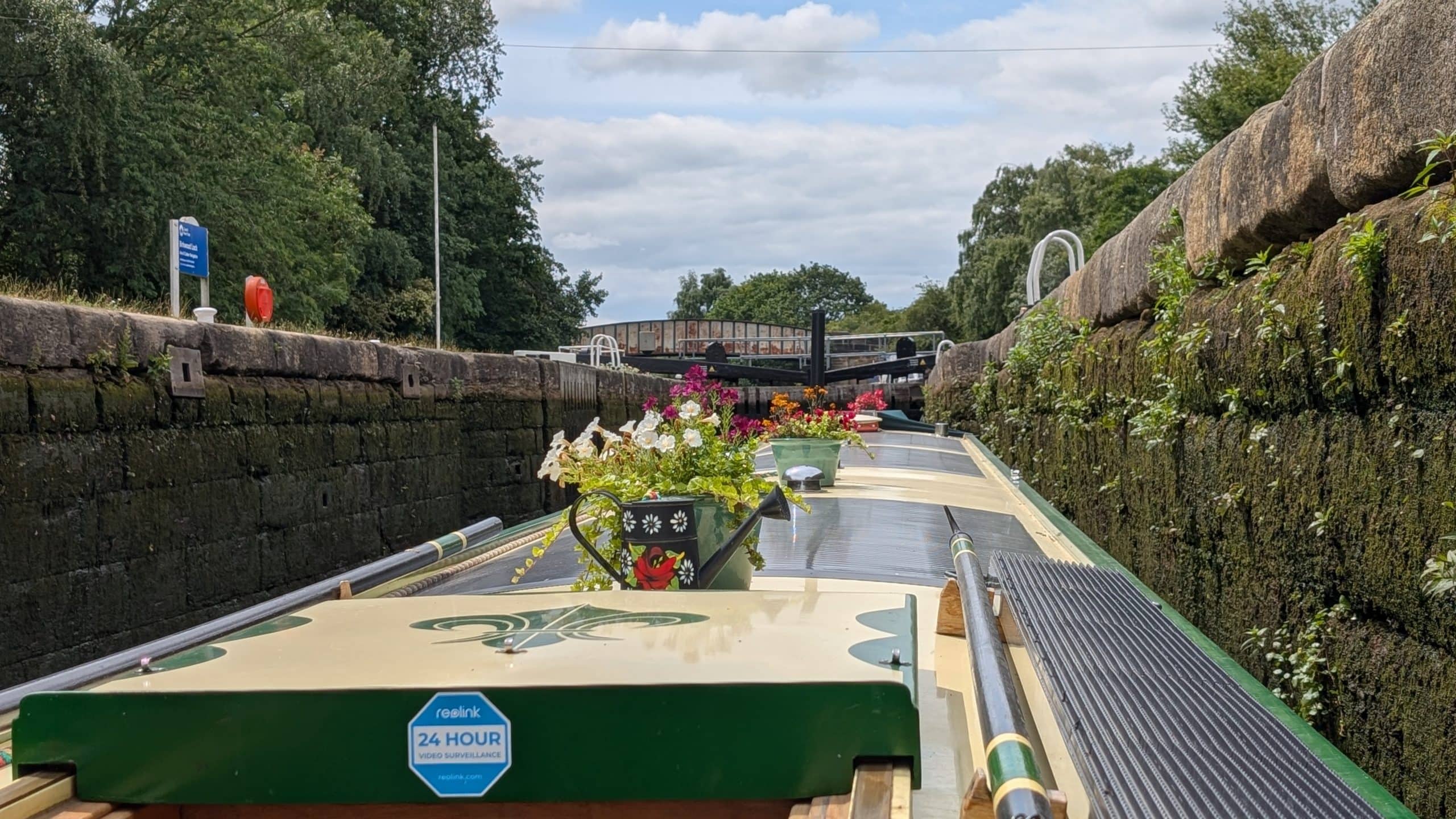 Narrowboat navigating through a canal lock with flowers on deck.