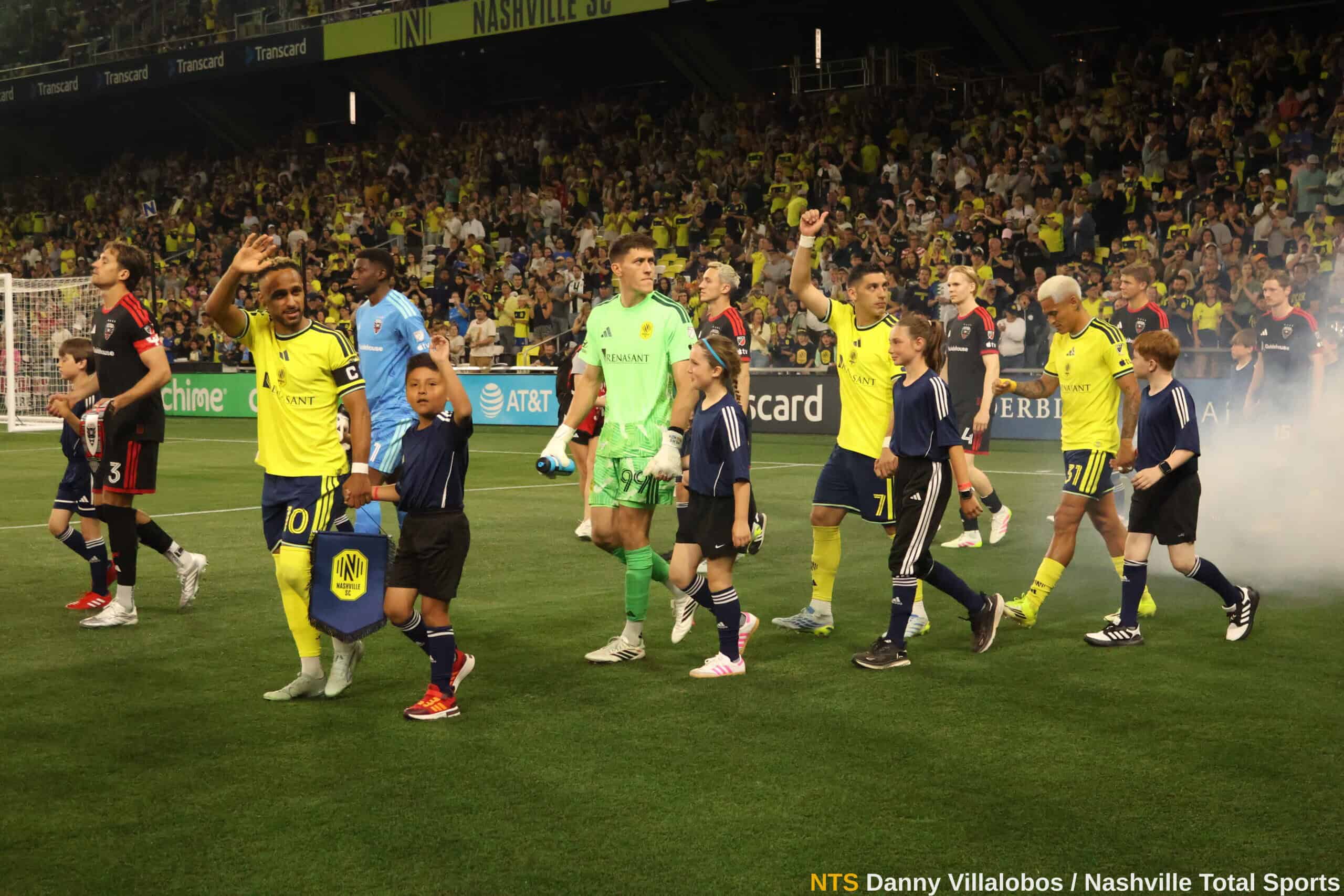 Jugadores de Nashville SC entran al campo acompañados de niños escoltas antes del partido vs DC United