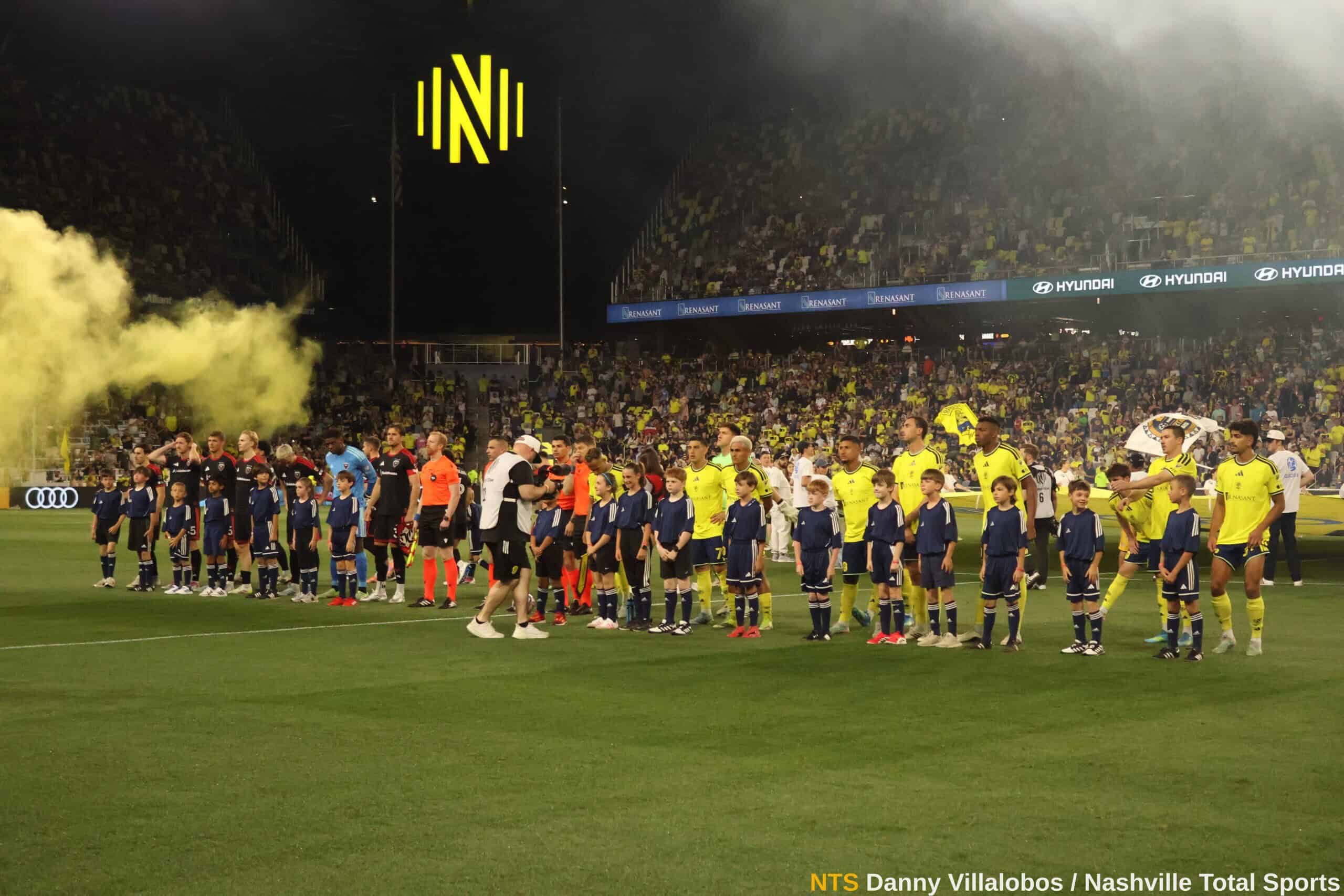 Jugadores de Nashville SC y DC United formados en el campo junto a niños escoltas antes del inicio del partido