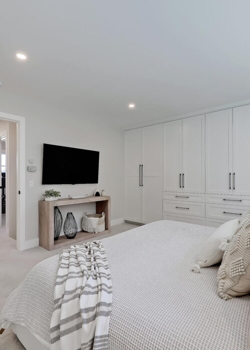 Bright modern bedroom with built-in storage, a wall-mounted TV, and cozy bedding in a new home.