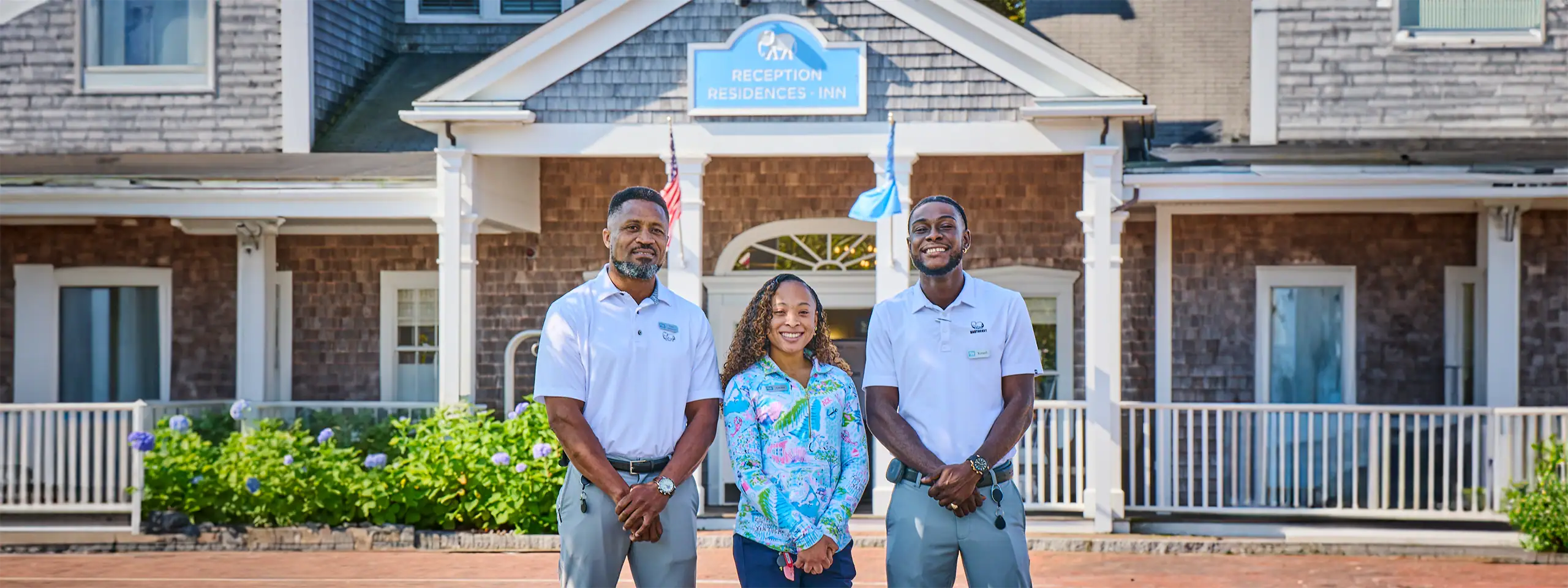 Three people standing in front of a residential building with a water fountain.