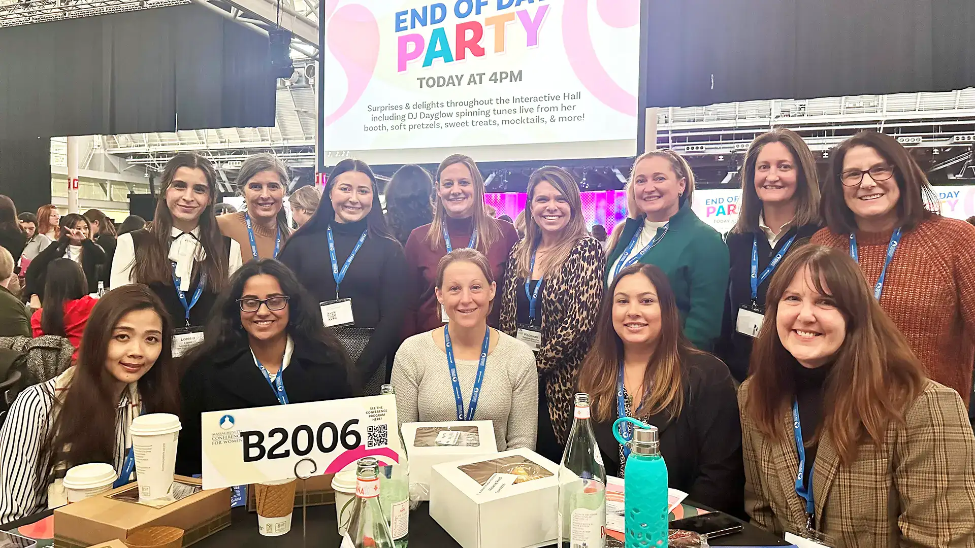 Group of women at a conference booth with a sign B2006 and an 'End of Day Party' banner.