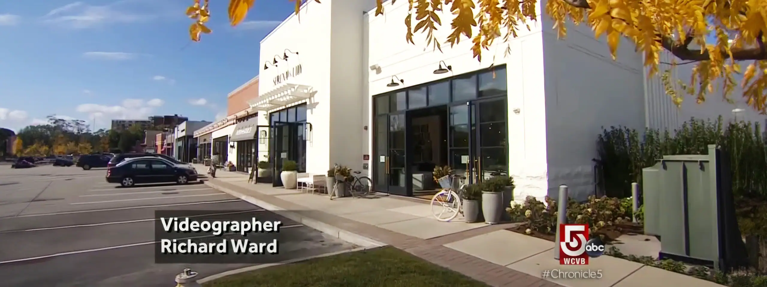 Exterior view of a retail shopping center with parked cars and autumn trees.