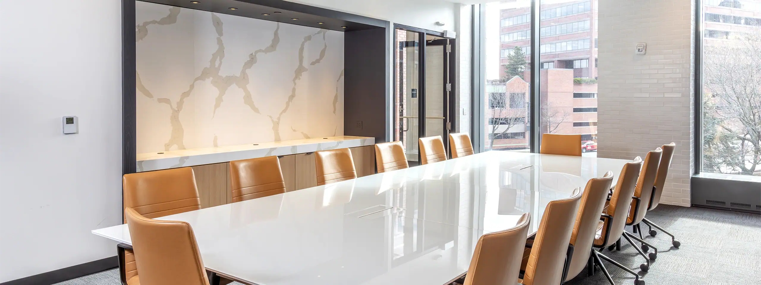 Modern conference room with a long white table and tan chairs near large windows.