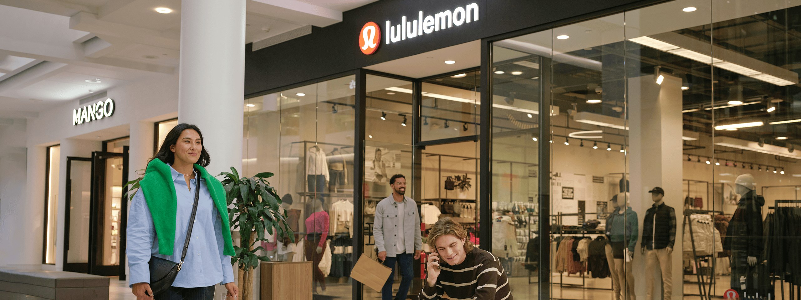 Shoppers walking past Lululemon and MANGO stores in a mall.
