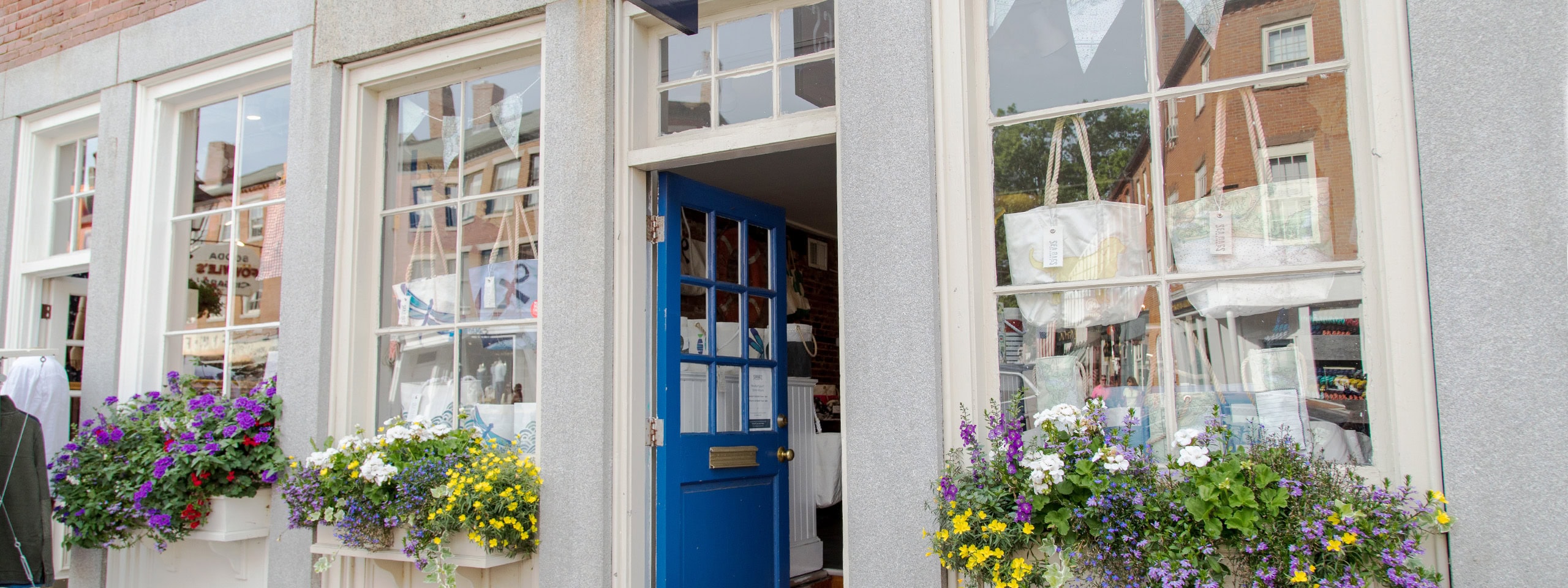 Colorful flower boxes outside a building with large windows and a blue door.