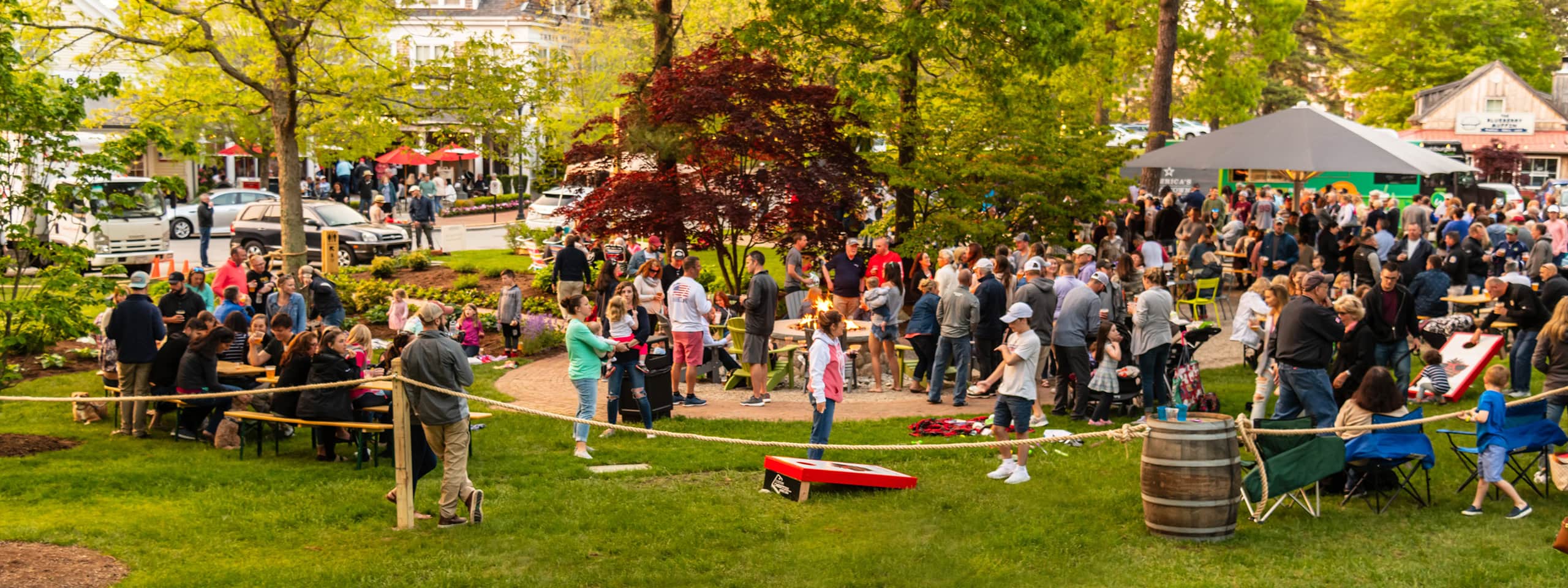 Crowd gathered at outdoor event in a park with trees and tents.