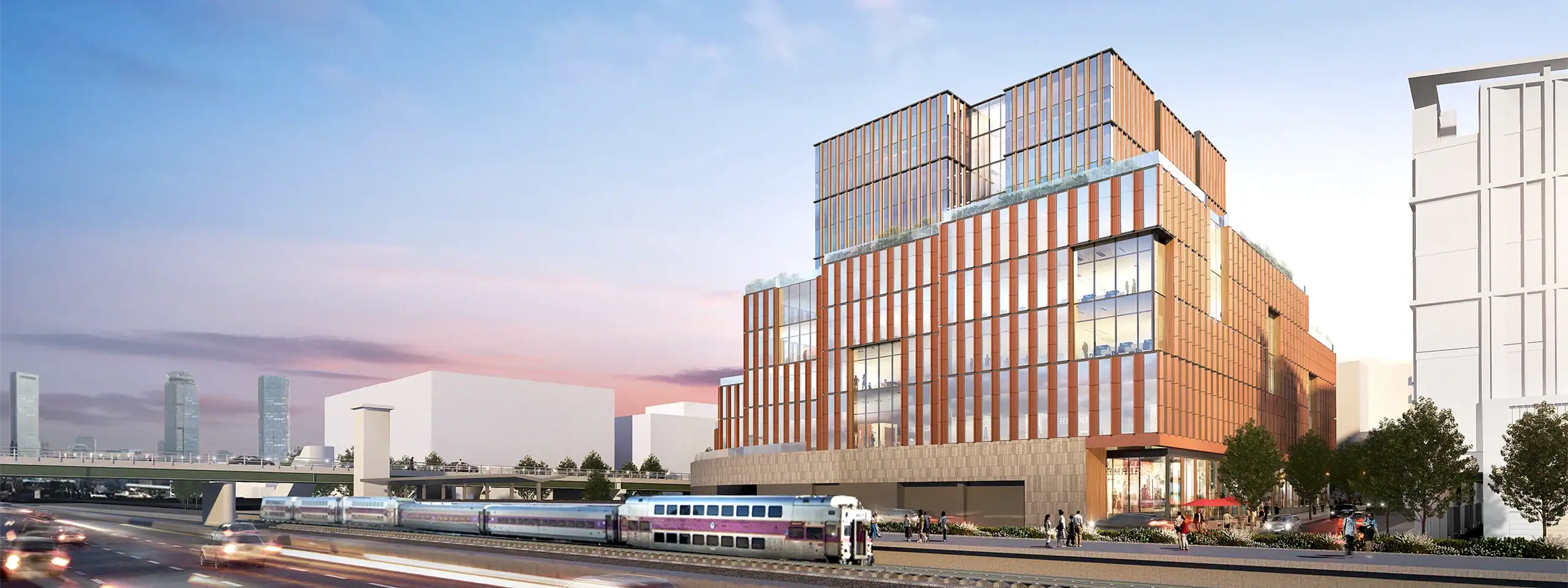 Modern multi-story building with glass and brick facade near train tracks in an urban setting.