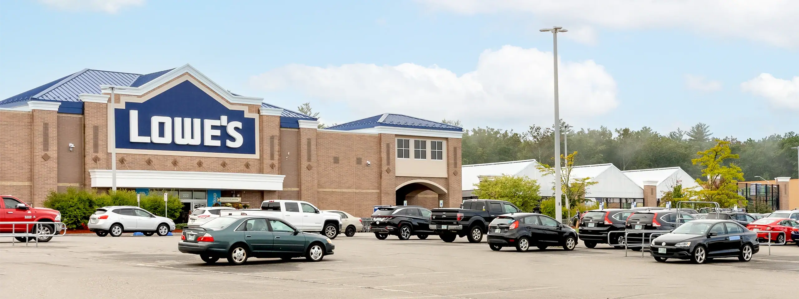 Lowe's store with parking lot and cars in front, clear sky, suburban setting.