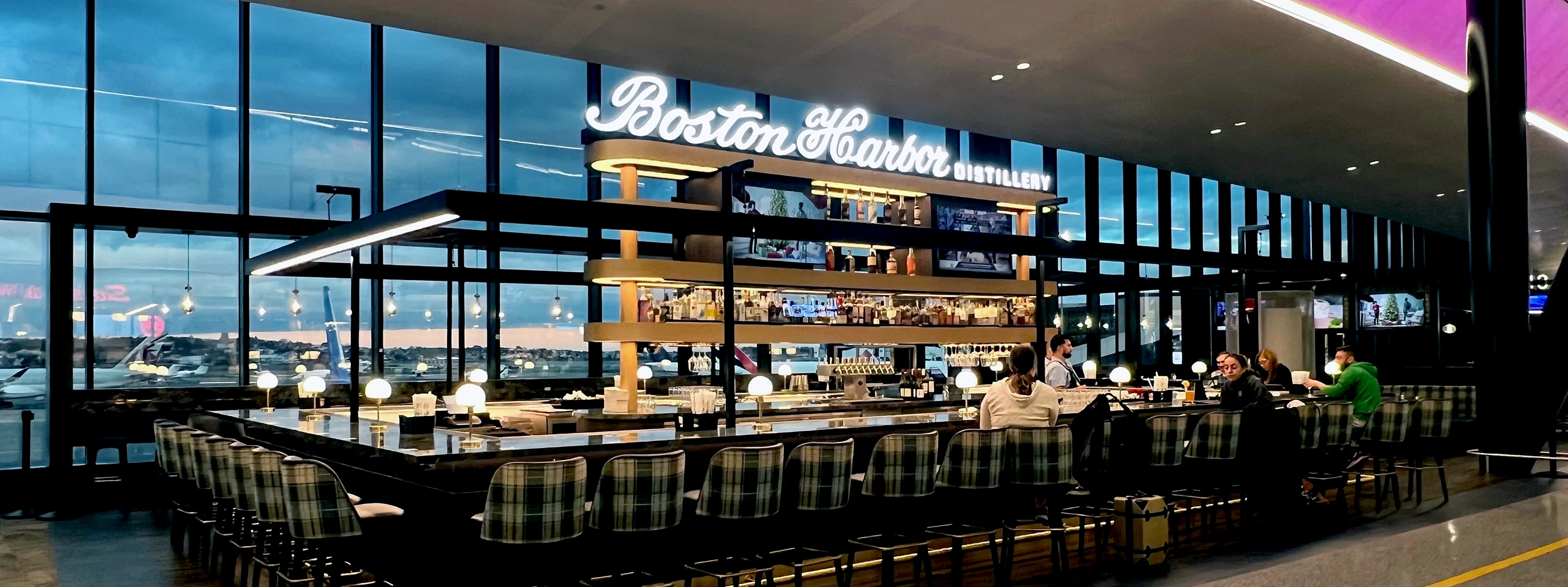 View of Boston Harbor from a modern airport lounge with seating and large windows.