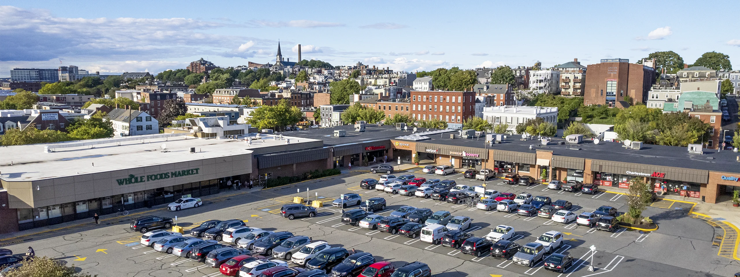 Large parking lot filled with cars outside a shopping center in a cityscape.